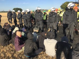 Aktivist*innen sitzend, Polizist*innen, stehend